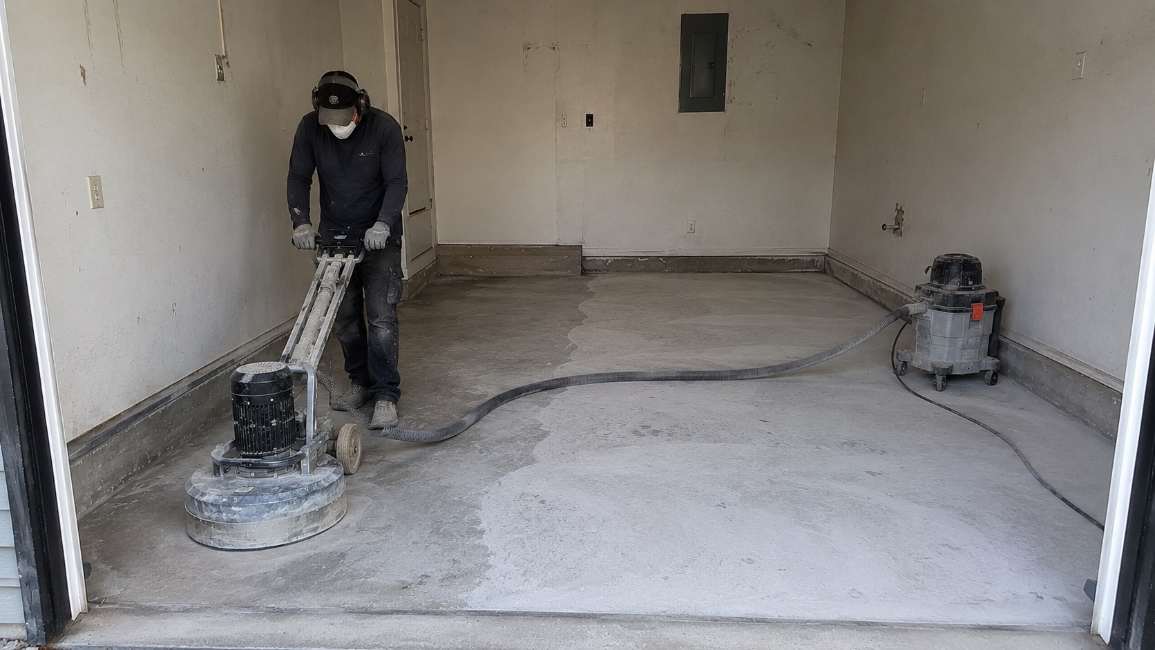 Contractor mechanically grinding a concrete garage floor during preparation